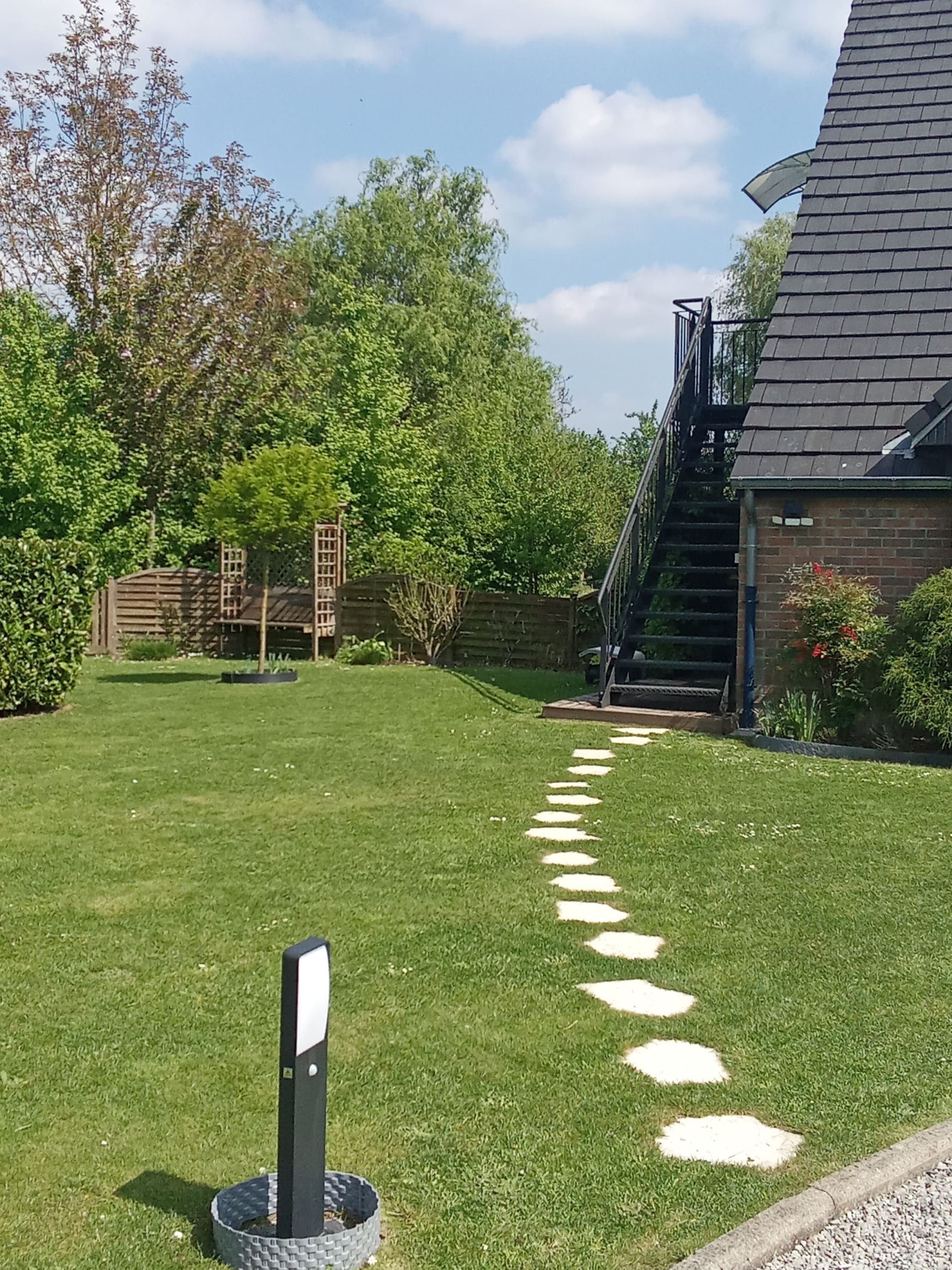 Le sol couvert d'herbe verte avec une ligne de pavé blanc en ligne les uns derrière les autres menant à un escalier métallique donnant sur les gîtes