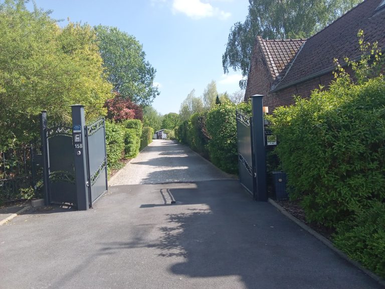 Portail ouvert sur une allée fleuris de chaque côté avec buisson bien taillé et cailloux blanc
